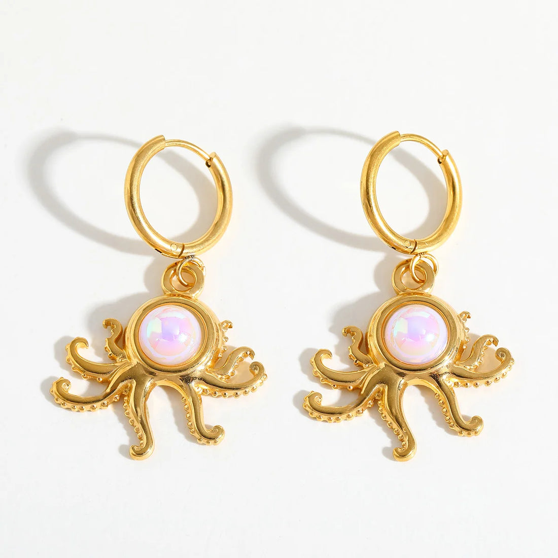 A pair of gold octopus drop earrings with iridescent white opal-like centers.