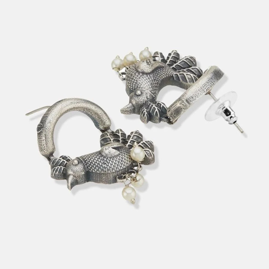 A pair of silver-toned statement earrings featuring textured fish designs with small white pearl-like bead accents, shown on a light gray background.