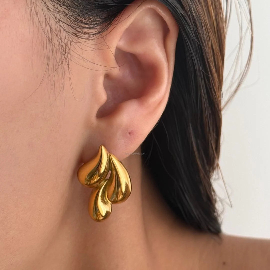 A close-up of a person's ear wearing a polished gold leaf-shaped stud earring.