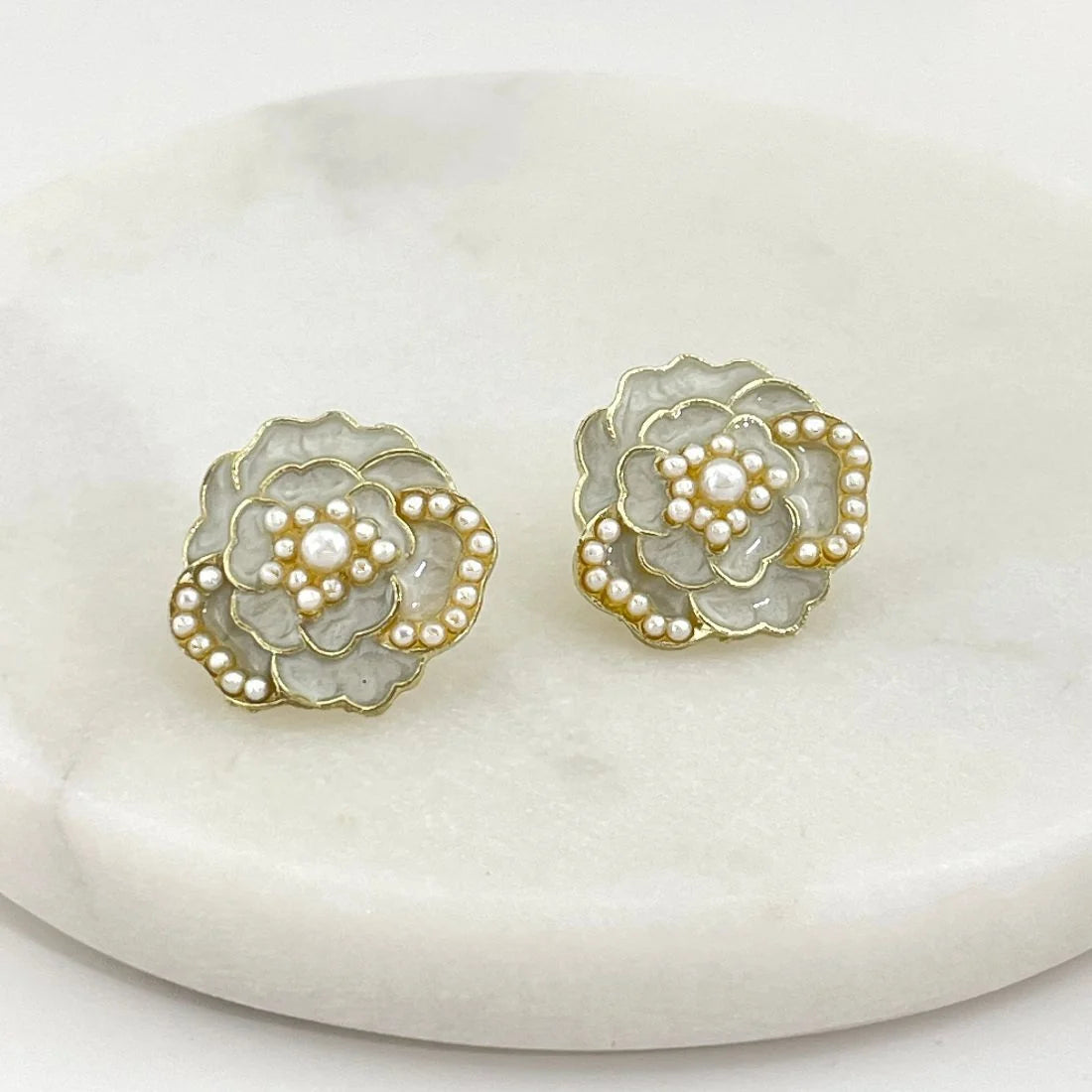 A pair of gold-tone flower-shaped earrings with white faux pearls, displayed on a round white marble surface.