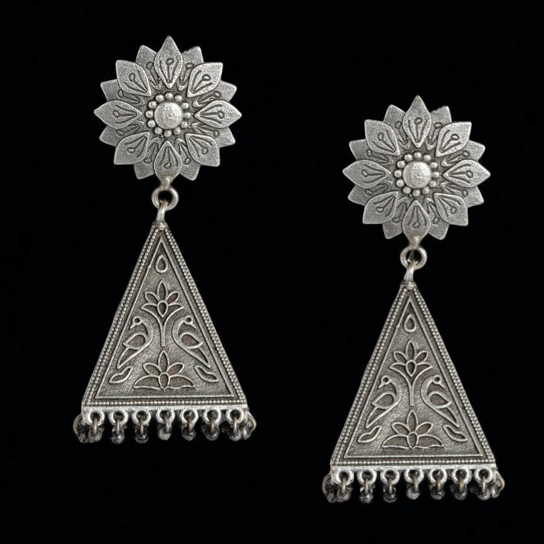A pair of silver-toned traditional Indian jhumka earrings with intricate filigree work, featuring a floral stud and a dangling triangular pendant with hanging bead tassels, set against a solid black background.