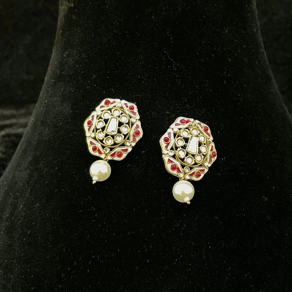 A pair of gold-plated Indian Kundan earrings with red stone accents and white pearl drops, displayed on a black velvet jewelry bust.