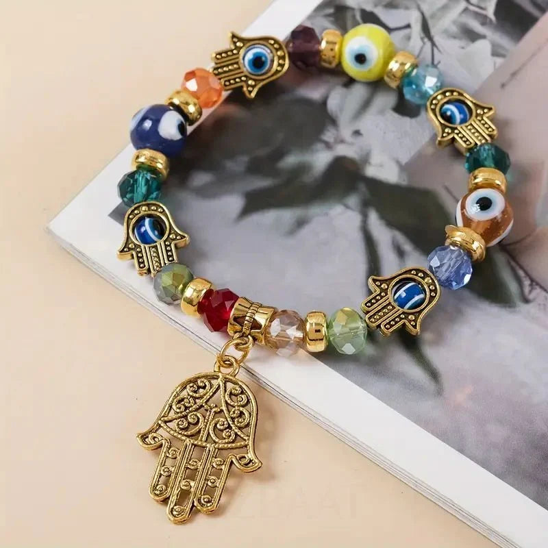Colorful beaded bracelet with gold Hamsa hand charms on a magazine background