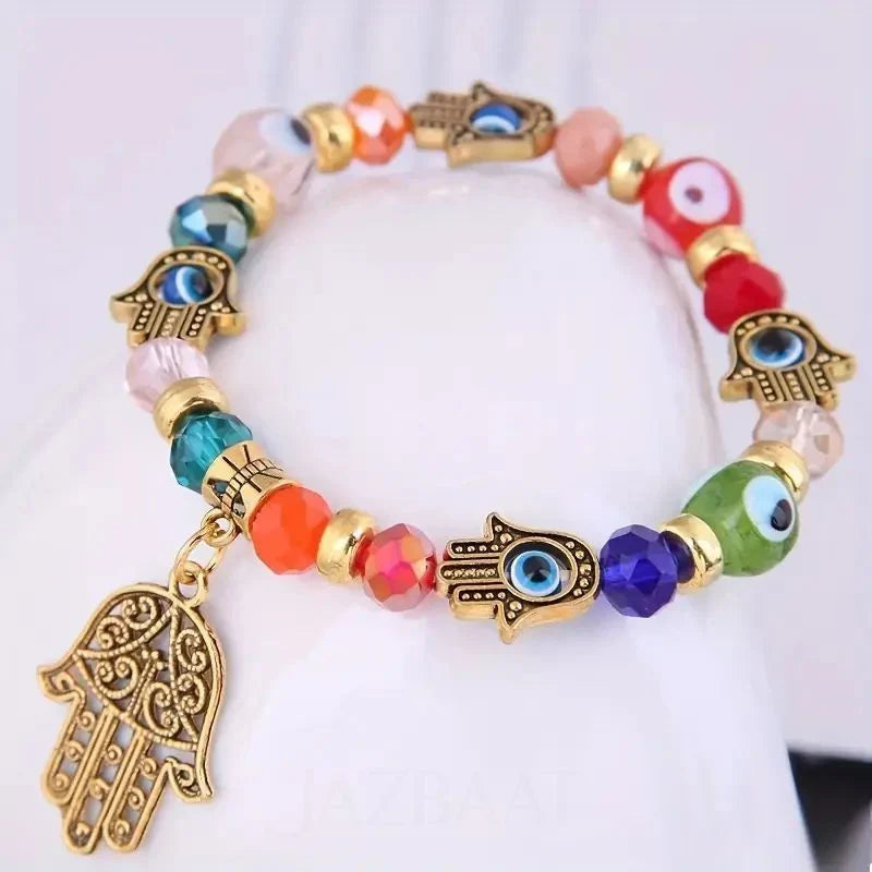 A colorful beaded stretch bracelet with gold-tone Hamsa charms, evil eye beads, and faceted glass beads in multiple colors, displayed on a white surface.