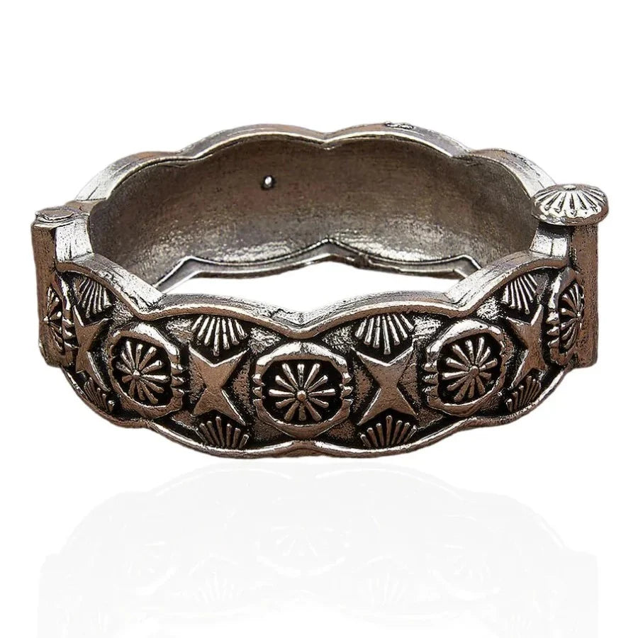 An antique bronze-toned metal bangle bracelet with intricate embossed patterns of stars, suns, and floral motifs, shown on a white background with a soft reflection.